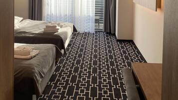 A hotel room with two beds, a patterned carpet, a flat-screen TV, and a window with curtains.