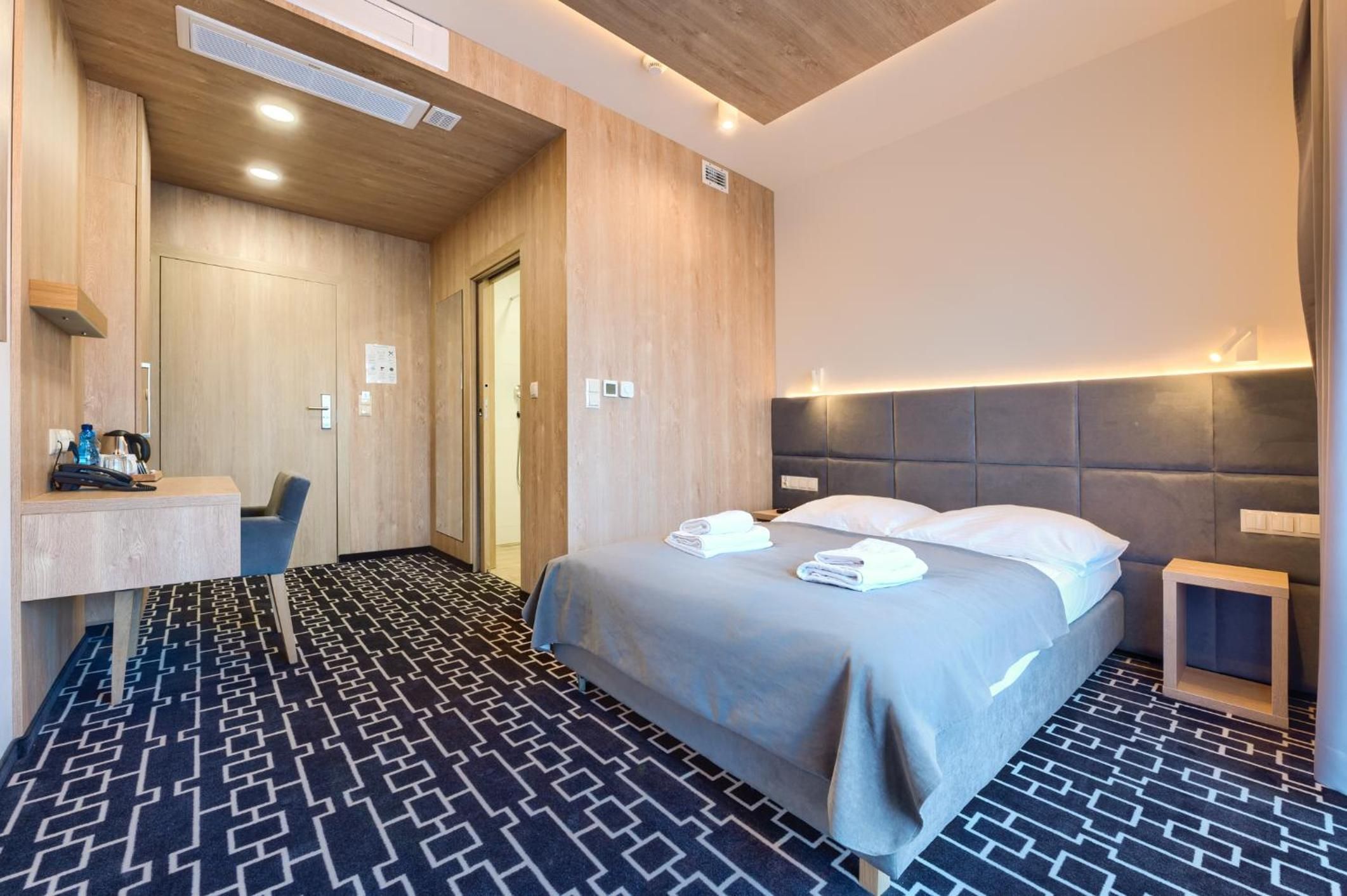 A hotel room with a bed, bedside table, and a desk with a chair.