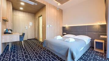 A hotel room with a bed, bedside table, and a desk with a chair.