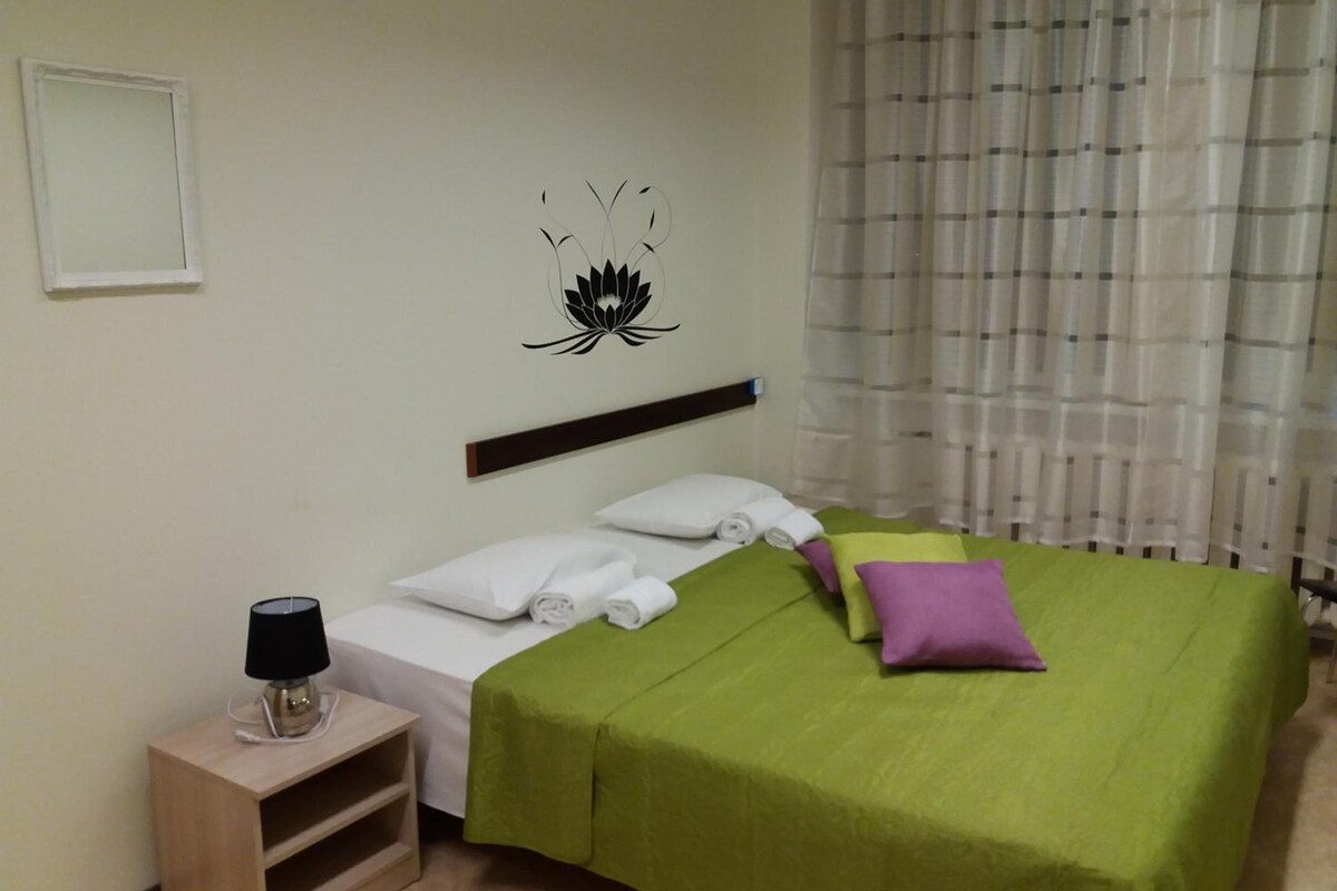 A hotel room with a bed, a nightstand, a lamp, a wall decoration, and a window with curtains.