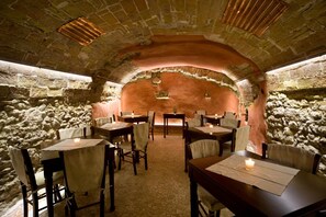 Un comedor subterráneo con paredes de piedra y mesas dispuestas para dos.