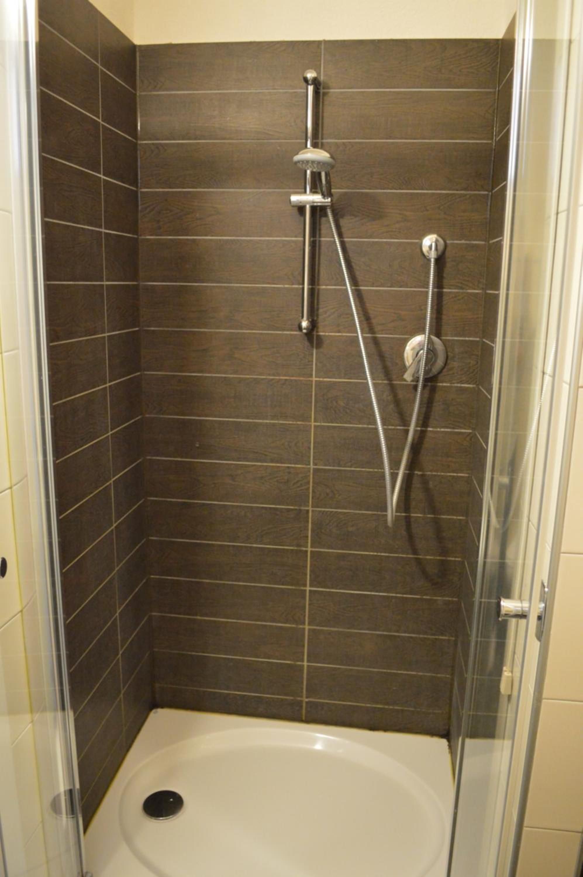 A shower stall with a glass door, a handheld showerhead, and a wall-mounted faucet.