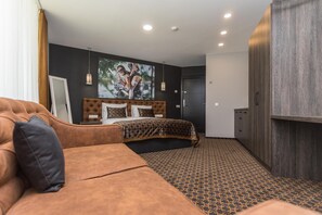 Quarto de hotel com uma cama grande, um sofá, um guarda-roupa e um quadro na parede.