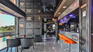 A modern bar area with a high ceiling, bar stools, and a seating area with tables and chairs. - Resort Hotel Elija (Palanga)