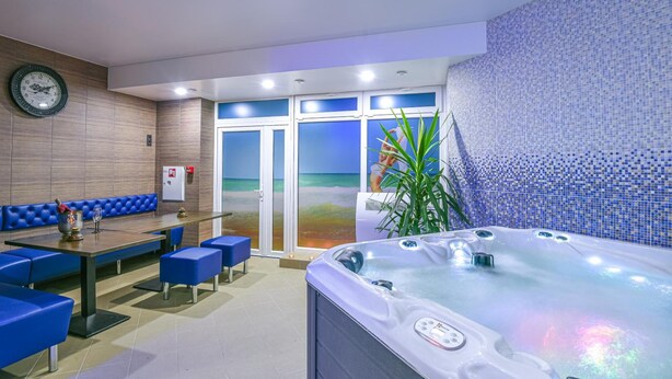 A hotel room with a hot tub, seating area, and a view of the beach through the glass doors. - Resort Hotel Elija (Palanga)