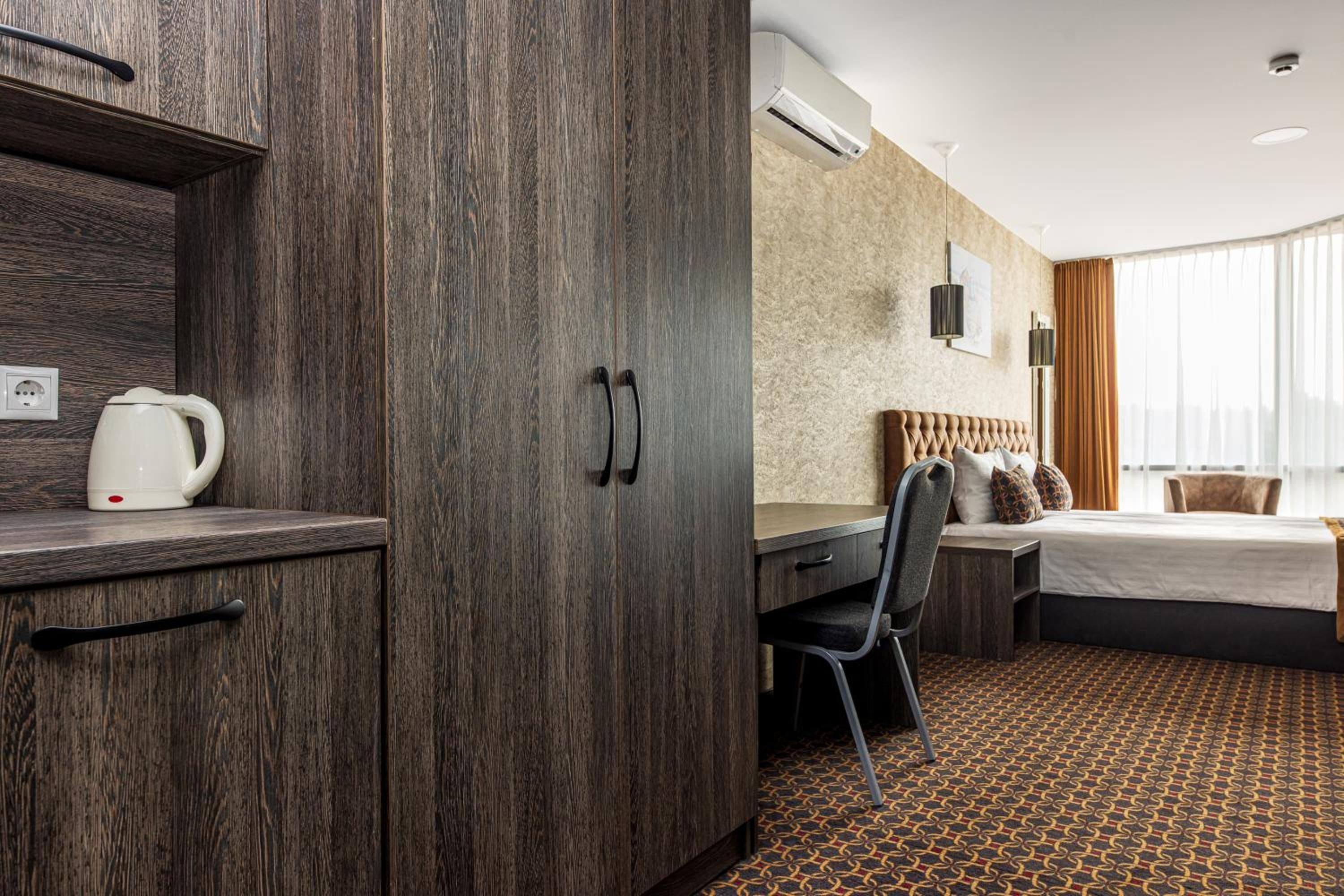 Ein Hotelzimmer mit Holzschrank, Schreibtisch, Bett und einem gemusterten Teppich.