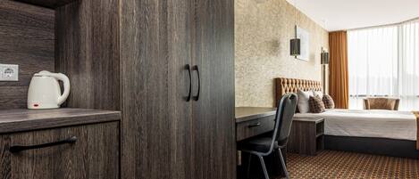 A hotel room with a wooden wardrobe, a desk, a bed, and a patterned carpet.