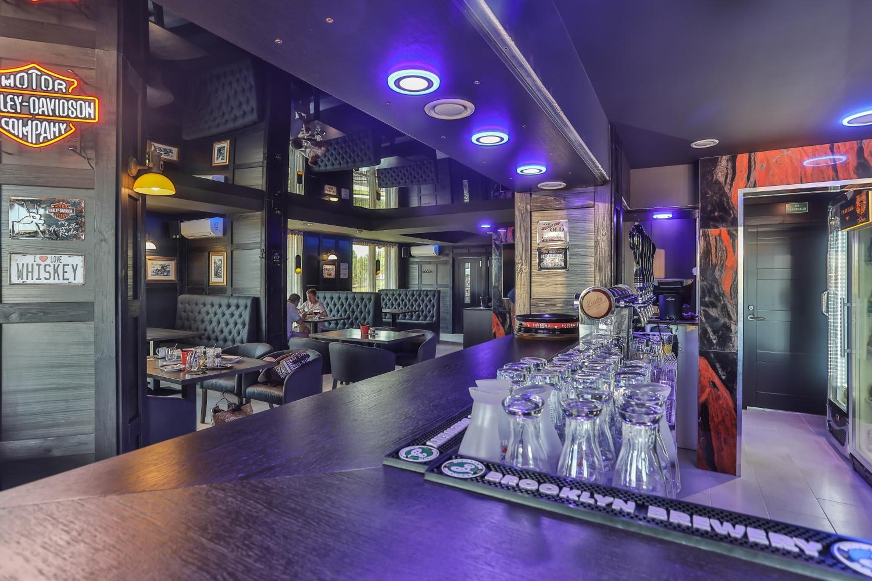A bar area with a counter, glasses, and a neon sign.