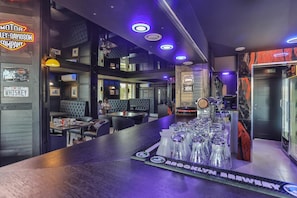 A bar area with a counter, glasses, and a neon sign.