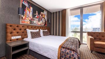 Ein Hotelzimmer mit einem großen Bett, einer Sitzecke, einem Bild an der Wand und Blick aus dem Fenster.