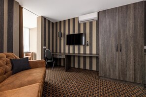 Habitación de hotel moderna con sofá, escritorio, silla, televisor de pantalla plana y armario.