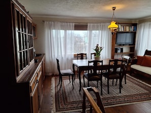 A dining area with a wooden table and chairs, a television, and a bookshelf.