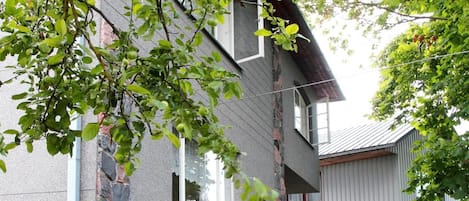 Un edificio de dos pisos con fachada de piedra, un pequeño jardín y un balcón visible.