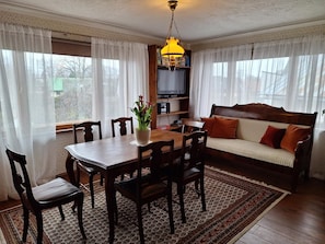 A cozy living room with a wooden dining table, chairs, a sofa, and a television.
