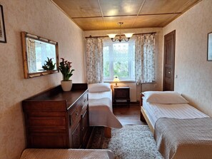 Habitación con dos camas, cómoda de madera, espejo, planta en maceta y ventana con cortinas.