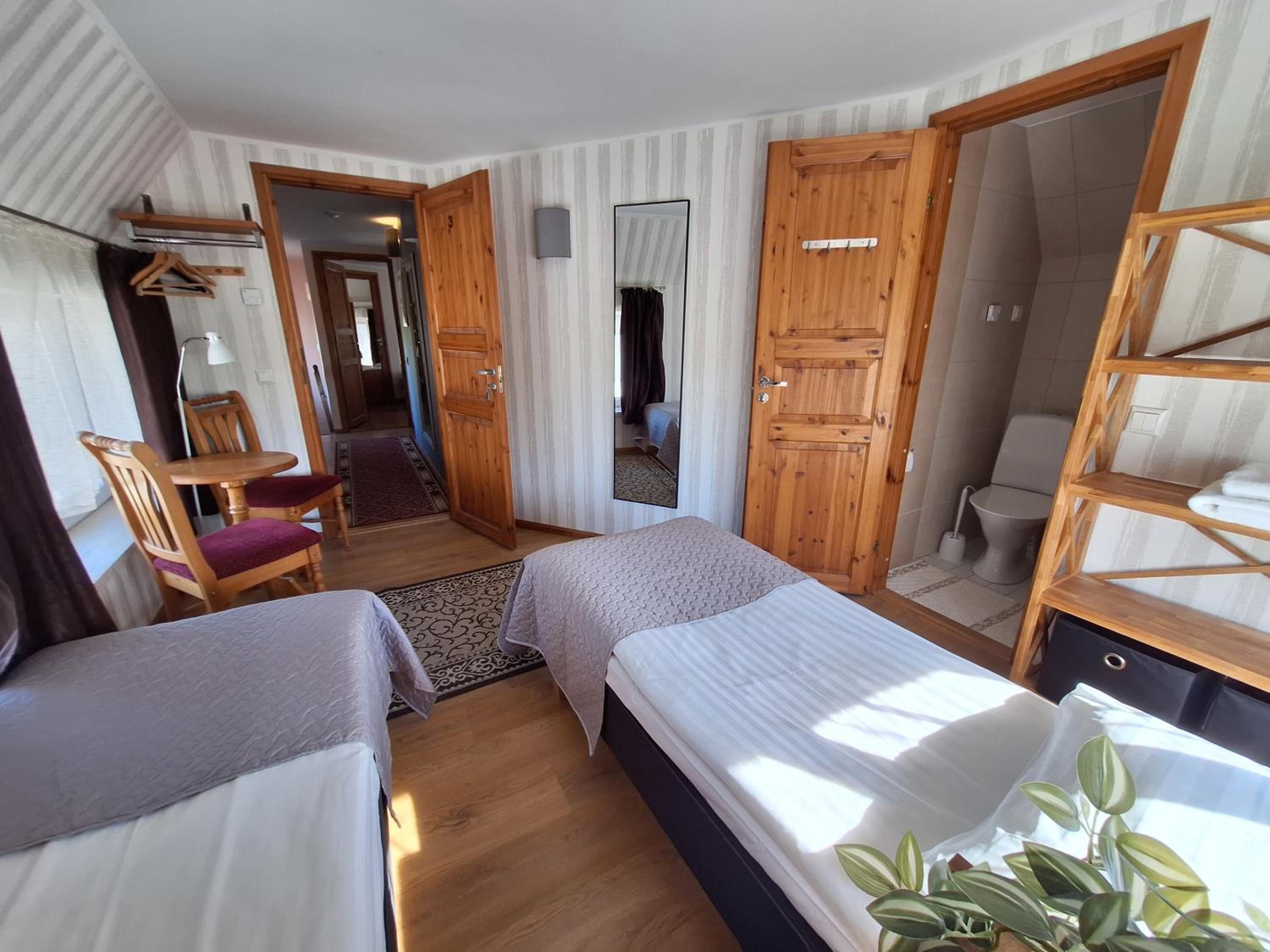 Habitación de hotel con dos camas, un armario de madera, un espejo, una silla y una mesita.