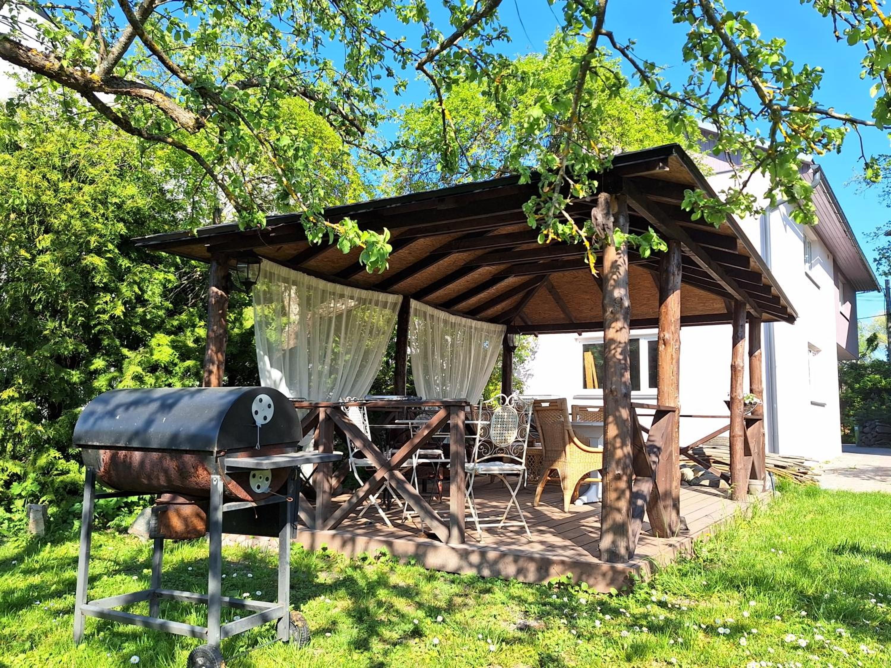 Un espacio al aire libre techado con una parrilla, mobiliario de mimbre y un edificio blanco al fondo.