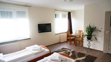 A hotel room with two single beds, a television, a dining table with chairs, a potted plant, and a radiator.