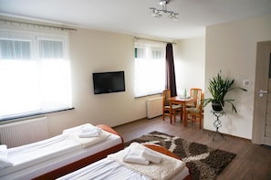 Una habitación de hotel con dos camas individuales, un televisor, una mesa de comedor con sillas, una planta en maceta y un radiador.