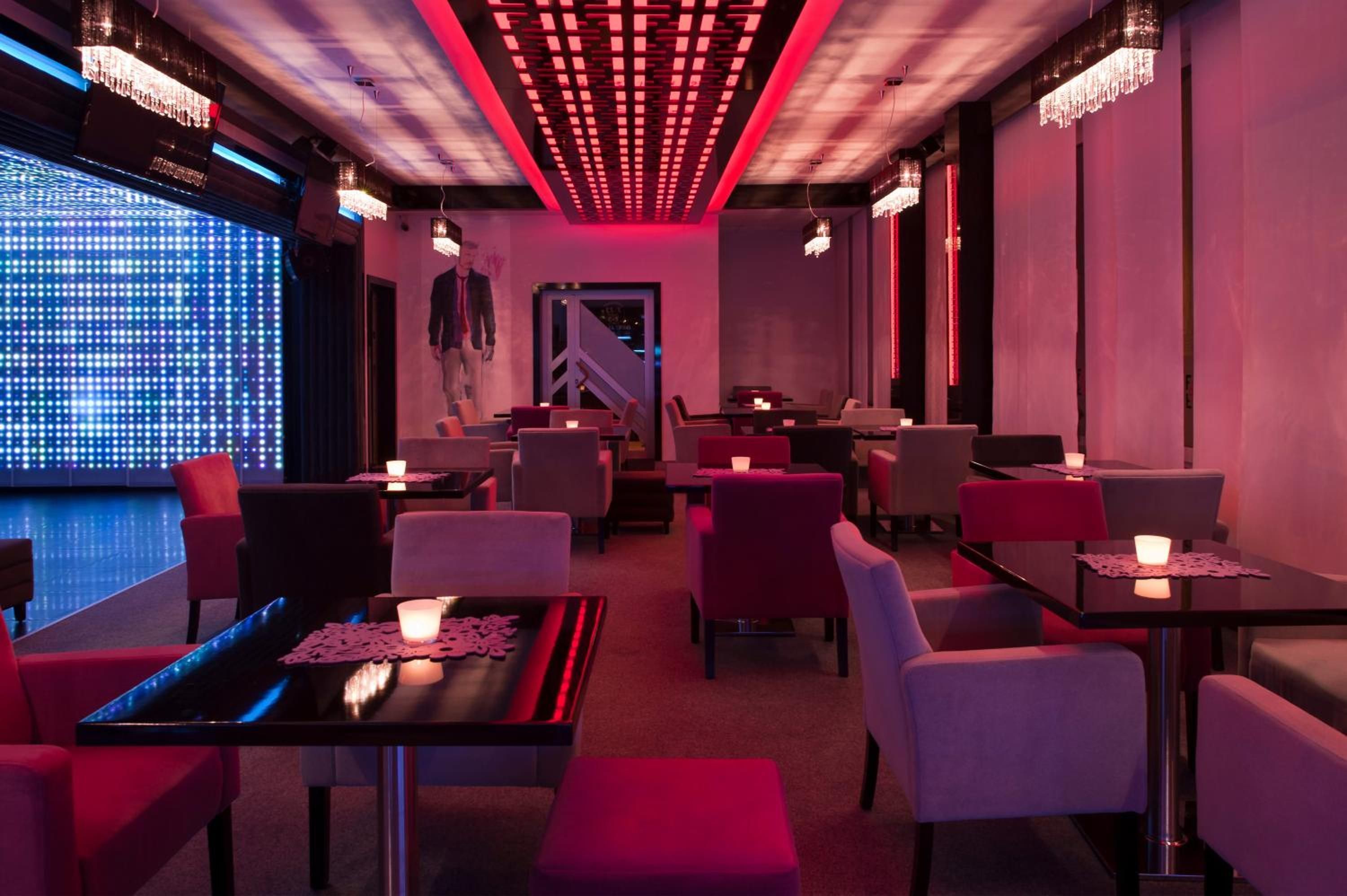 A modern restaurant interior with ambient lighting, tables with candles, and a digital display on the left.