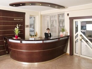 Un mostrador de recepción con una recepcionista, una planta y un letrero que dice 'RECEPTION'.