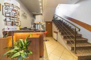 A hotel reception area with a counter, a staircase, and a wall with framed pictures. - Hotel Doris (Oborniki)