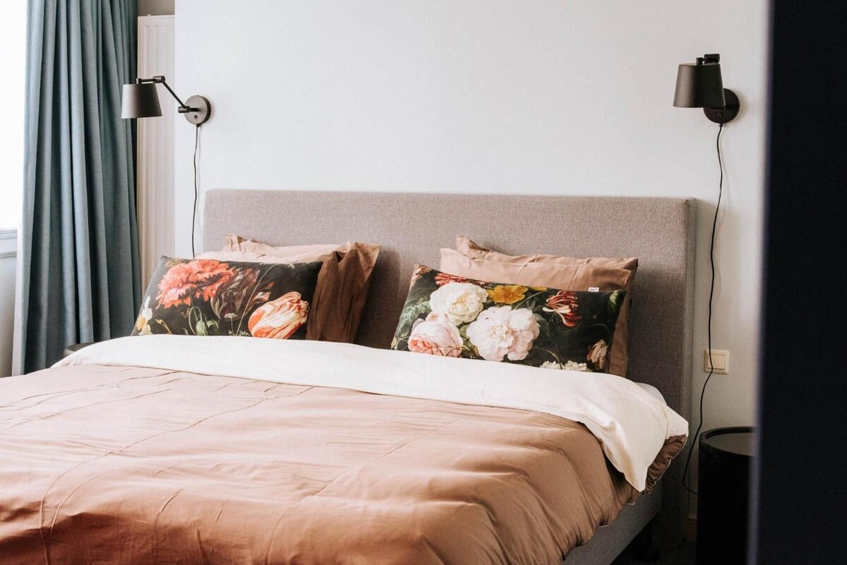 A bed with floral pillows, a grey headboard, and two bedside lamps.