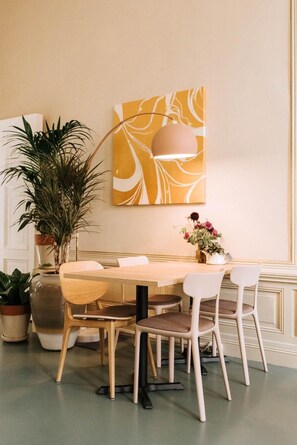 A dining area with a round table, four chairs, a potted plant, a vase with flowers, and a wall-mounted lamp. - Stadshotel Steegoversloot (Dordrecht)