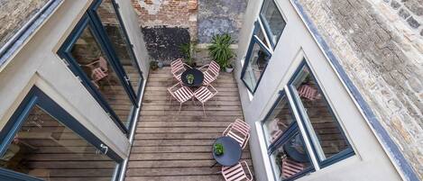 Una terraza en la azotea con piso de madera, una mesa redonda y sillas rosadas.