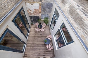 Una terraza en la azotea con piso de madera, una mesa redonda y sillas rosadas.