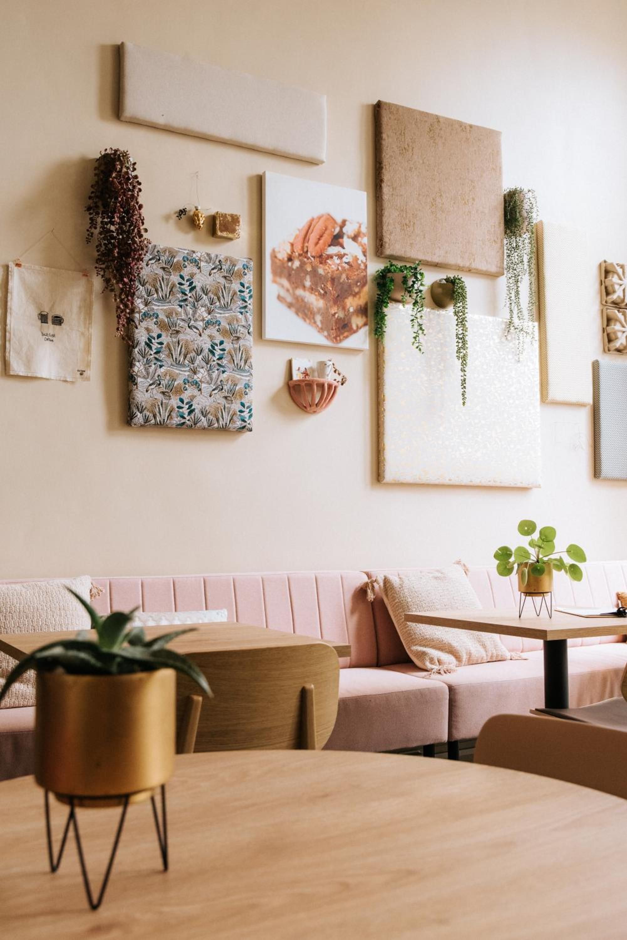 Une pièce chaleureuse avec une table en bois, un canapé rose et divers éléments décoratifs, notamment une estampe à motifs floraux et un tableau sur le thème de la nature.