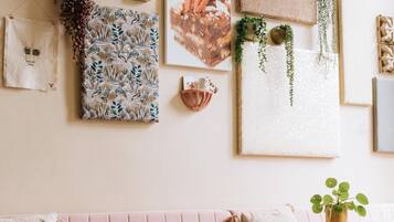 Une pièce chaleureuse avec une table en bois, un canapé rose et divers éléments décoratifs, notamment une estampe à motifs floraux et un tableau sur le thème de la nature.