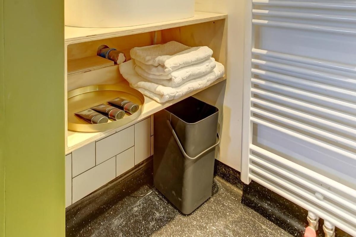 A bathroom with a white sink, mirror, and towel rack. There is a trash bin and a towel dispenser on the counter.