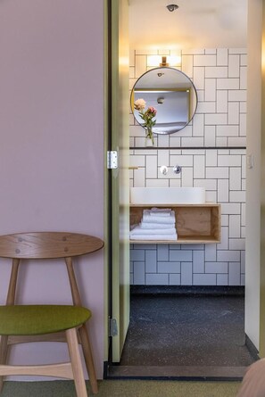 Un baño con espejo, lavamanos y un pequeño estante de madera con toallas.
