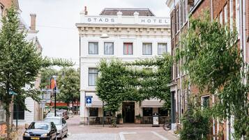 Une vue de la rue où se trouve l’hôtel Stads, avec une chaussée pavée, des voitures garées et les bâtiments environnants.