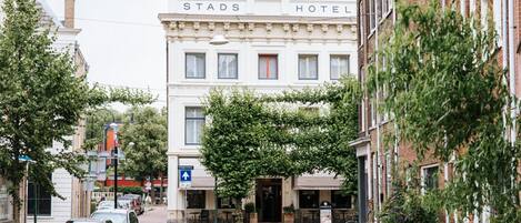 Vista de la calle del Hotel Stads, con un adoquín, coches estacionados y edificios circundantes.