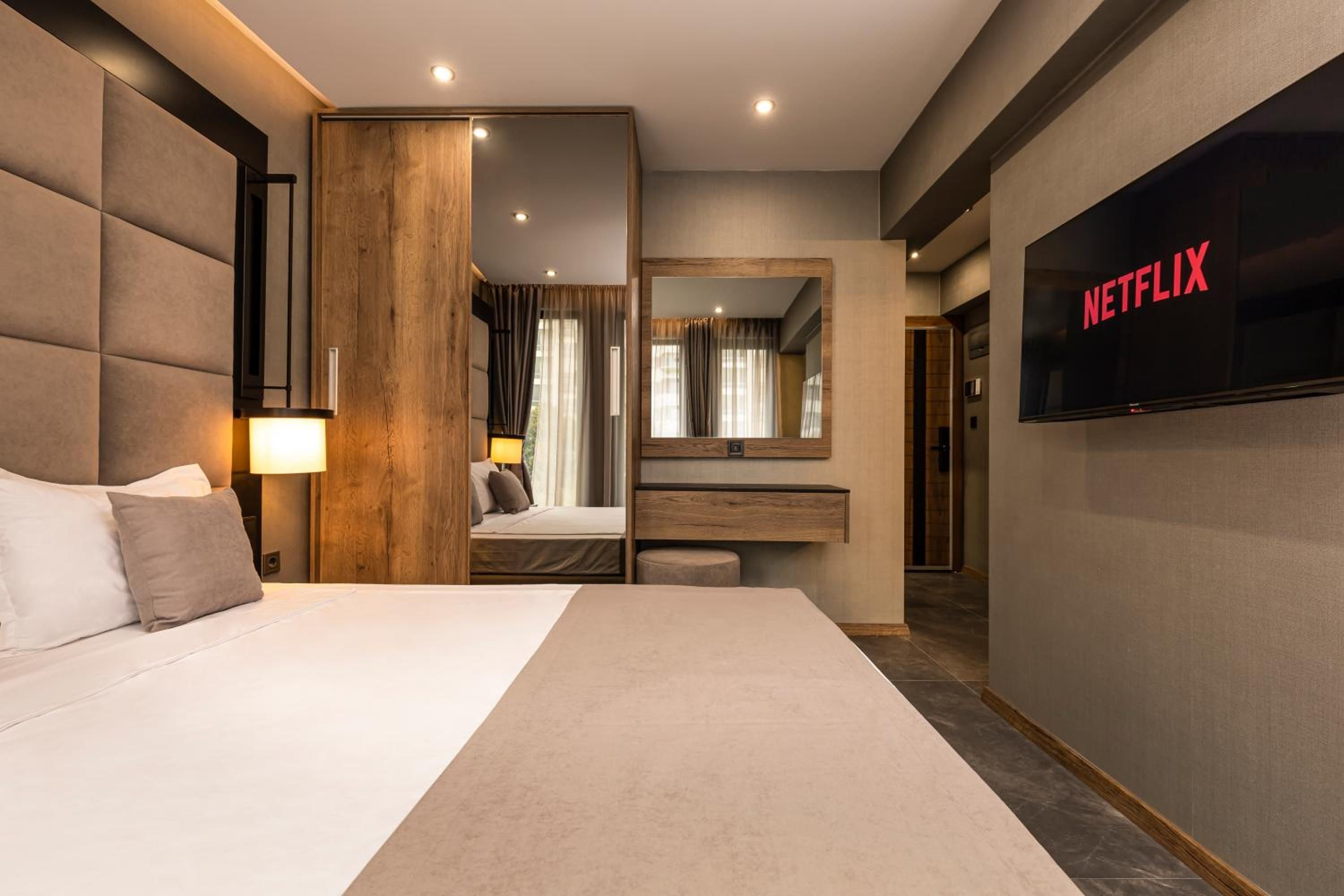 A modern hotel room with a large bed, a TV mounted on the wall, and a wooden panel design.