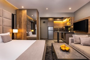 A modern hotel room with a bed, a sofa, a coffee table with fruit, a kitchen area, and a TV mounted on the wall. - Soho Apart House (Plovdiv)