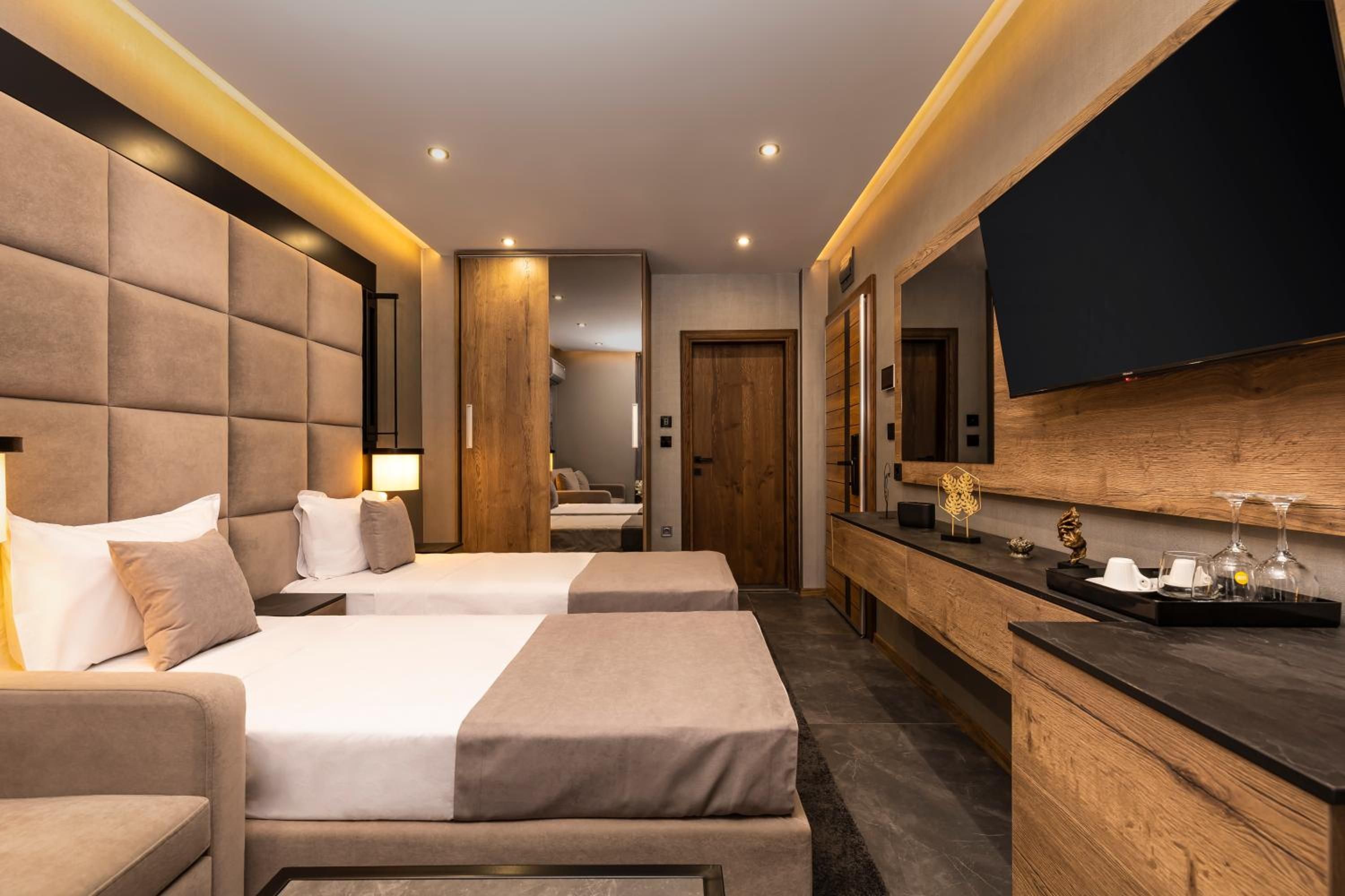 A hotel room with two beds, a large mirror, a flat-screen TV, and a wooden sideboard with a tray.