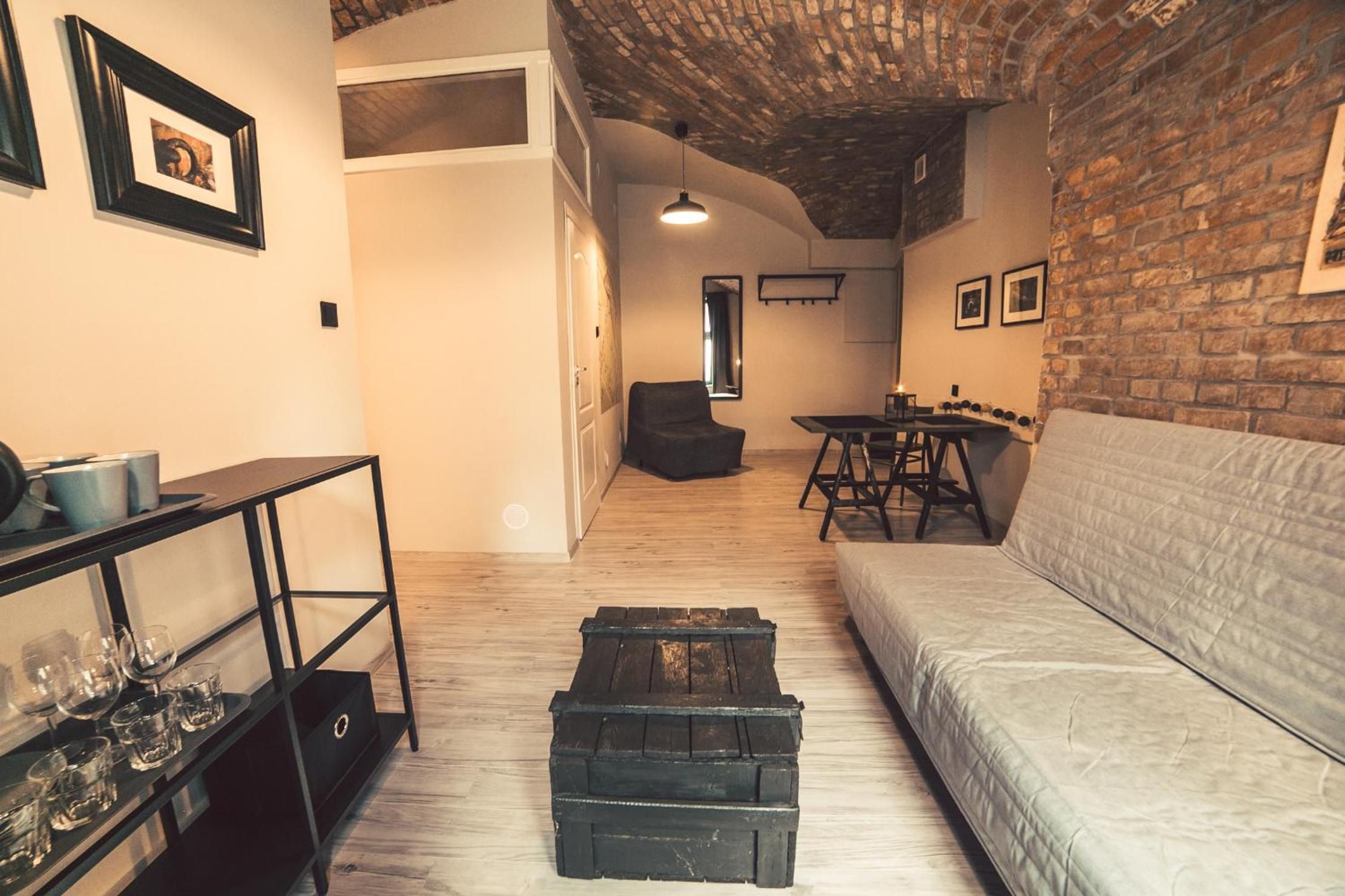 Ein gemütliches Wohnzimmer mit einer Couch, einem Couchtisch und einem Essbereich mit Tisch und Stühlen. An den Wänden hängen Bilder und eine Wand ist aus Backstein.