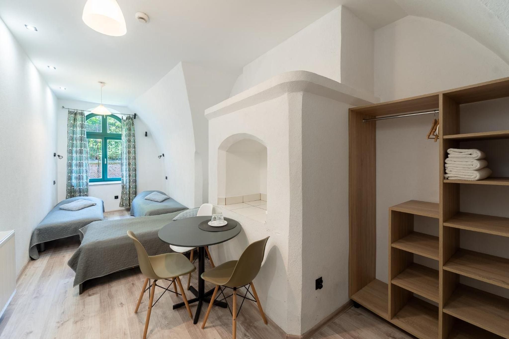 A compact room with a bed, two chairs, a table, and a wooden wardrobe.