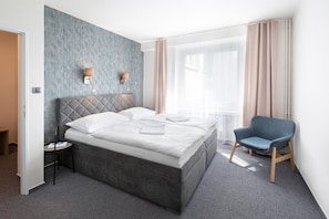 Quarto de hotel moderno com uma cama grande, uma cadeira e uma janela com cortinas.