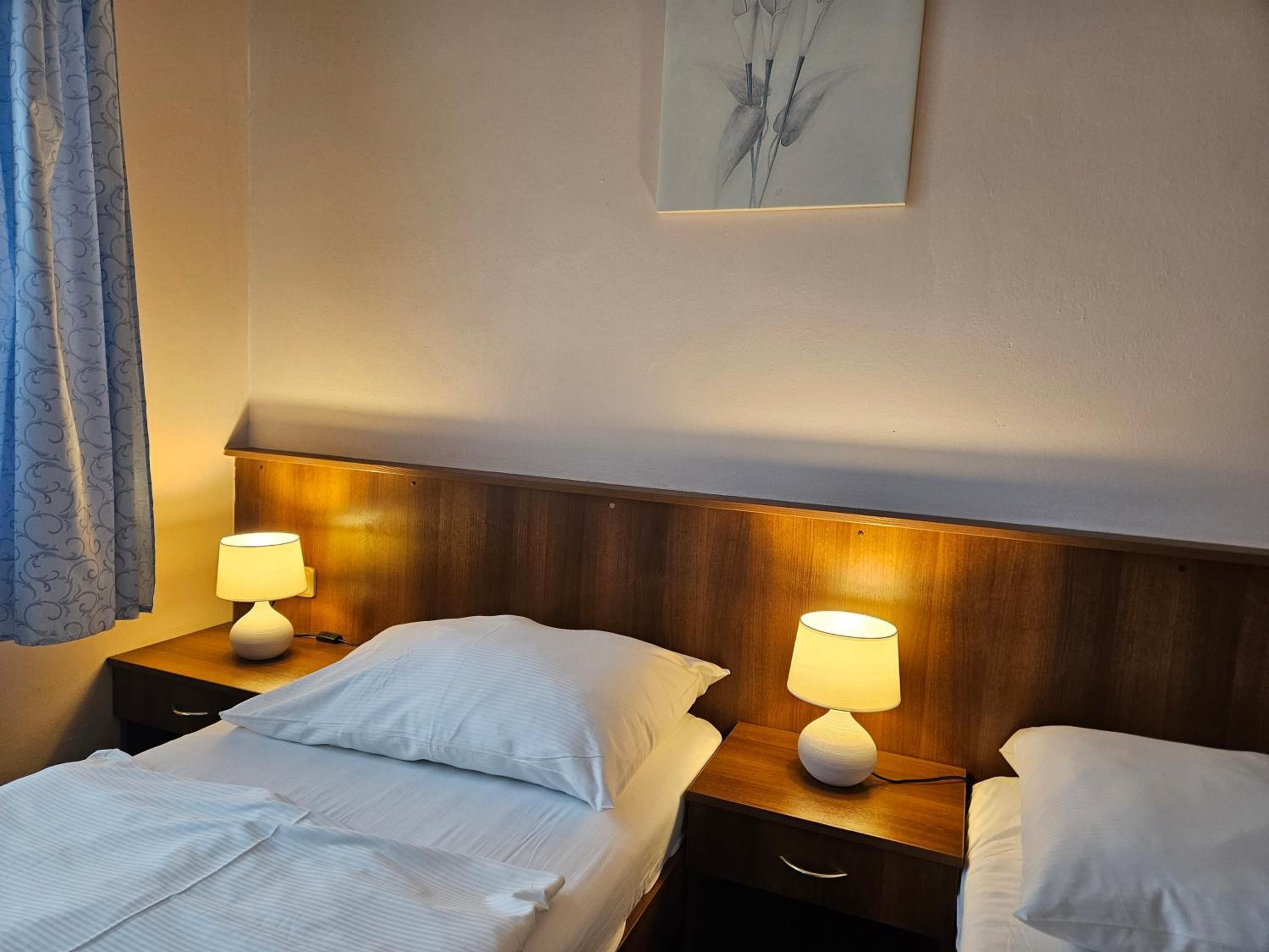Ein Hotelzimmer mit zwei Betten, jeweils mit weißen Laken, Holz-Kopfteilen und Nachttischlampen.
