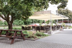 An outdoor seating area with tables and chairs, a covered section, and a picnic table. - Hotel Trim (Pardubice)