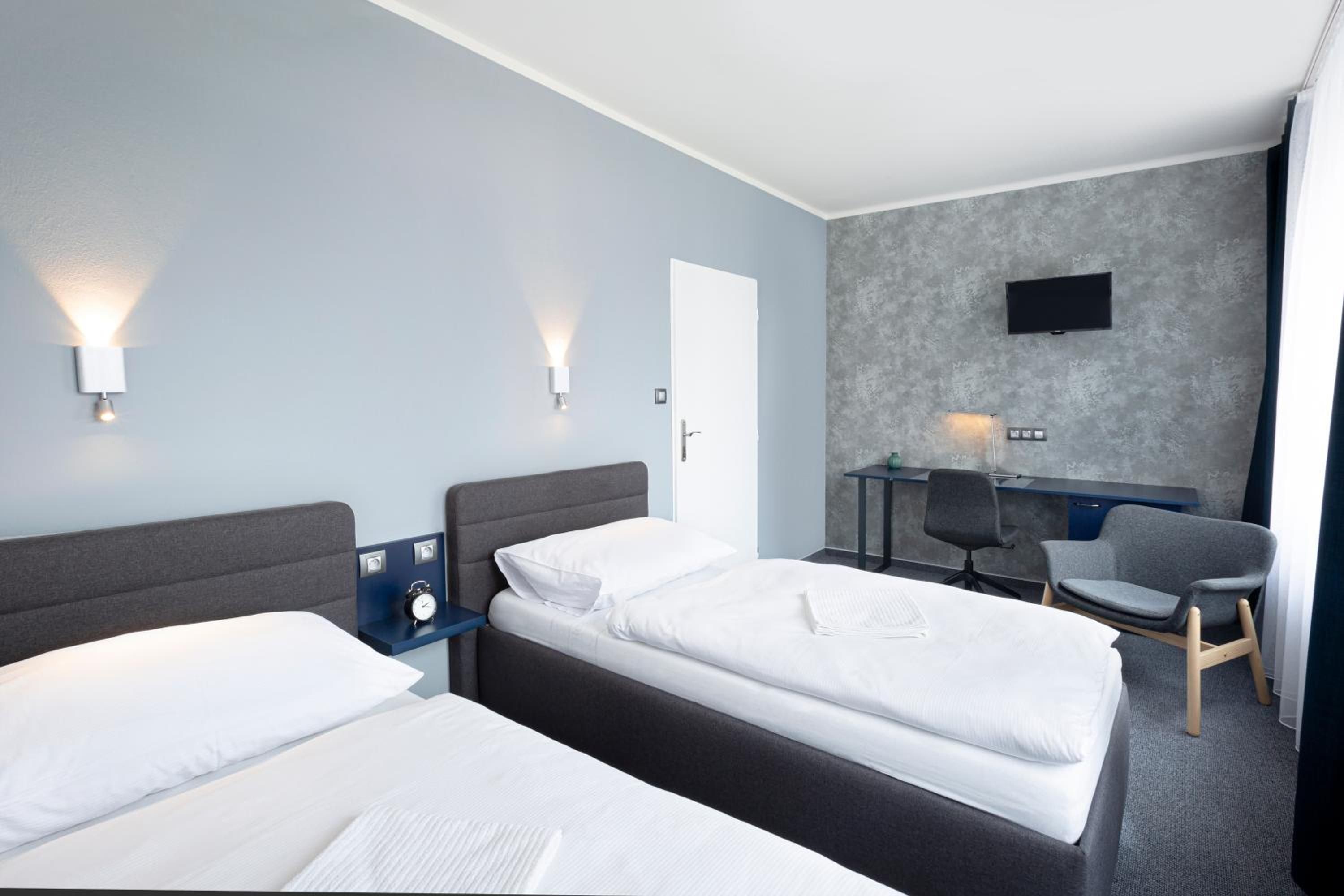 Una habitación de hotel con dos camas, un escritorio, una silla y un televisor montado en la pared.