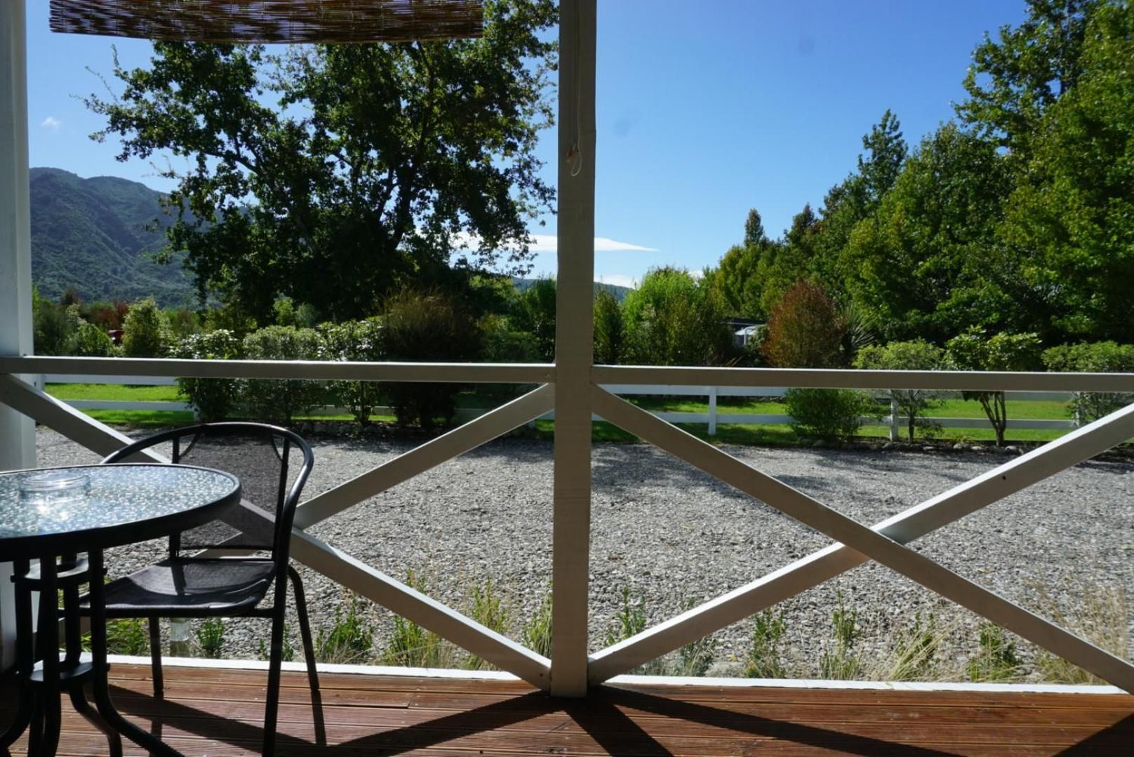 A covered outdoor area with a table and chairs, a view of a gravel path, and a white fence.