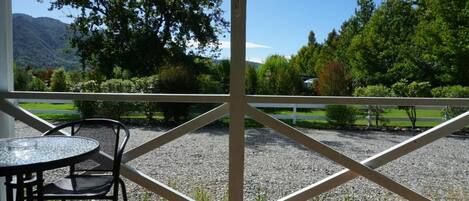 A covered outdoor area with a table and chairs, a view of a gravel path, and a white fence.