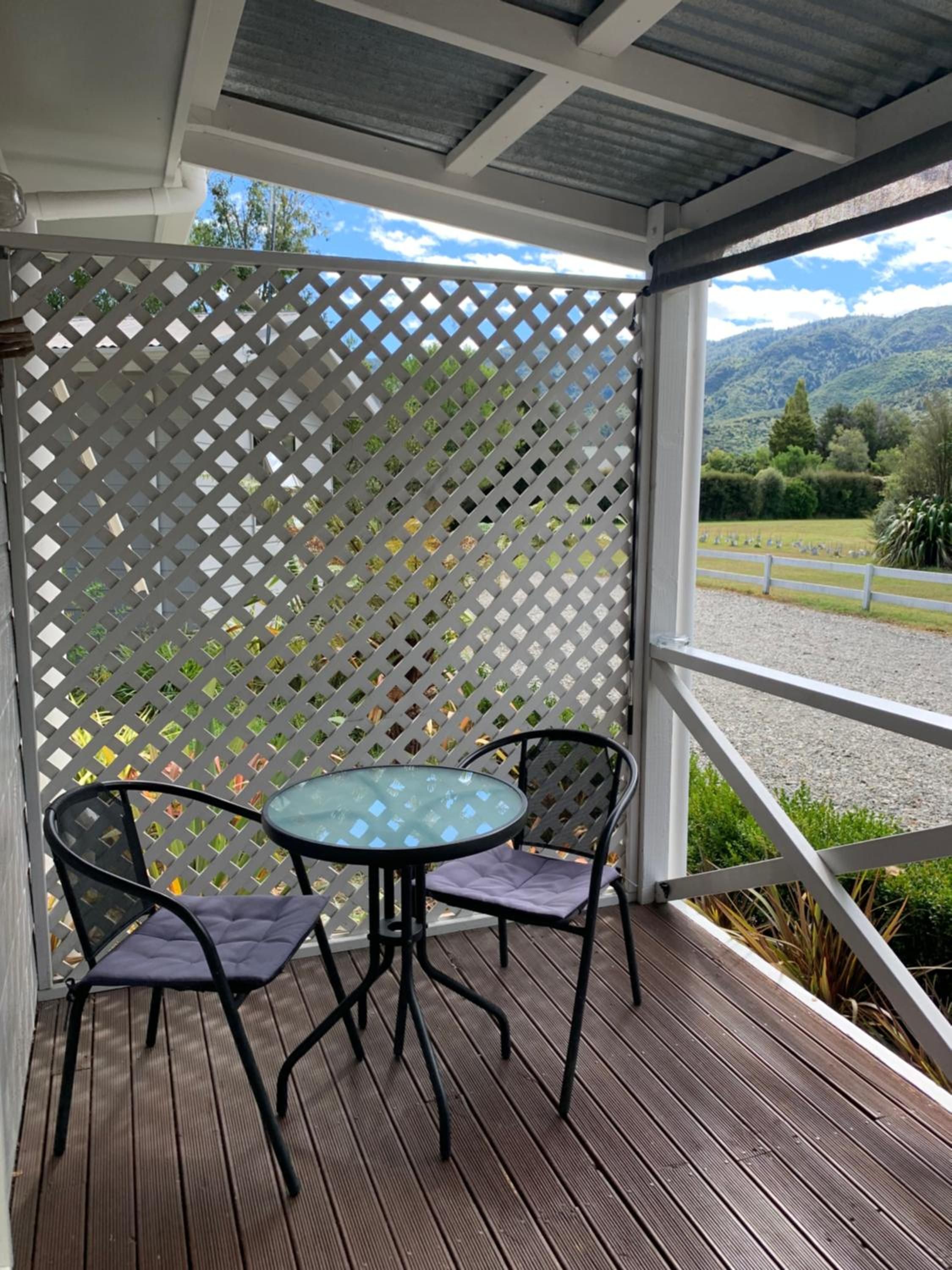 A covered outdoor seating area with a table and chairs, a lattice screen, and a view of a rural landscape.