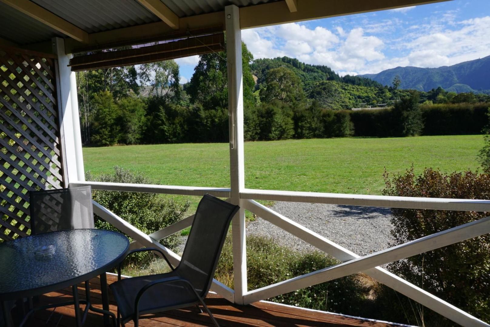 Ein überdachter Außenbereich mit Tisch und Stühlen, mit Blick auf ein grünes Feld und Berge.