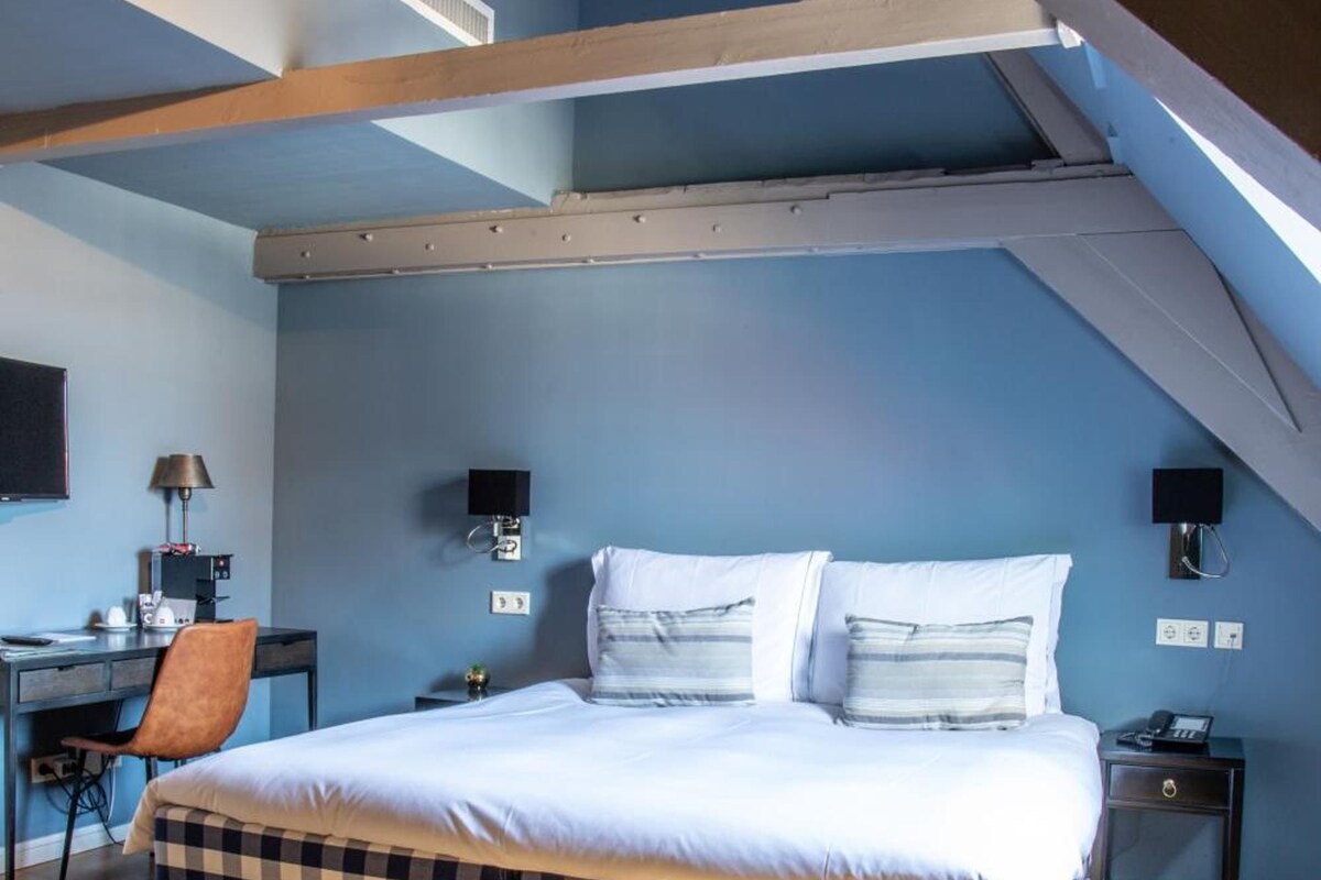 A bedroom with a checkered bedspread, a desk with a chair, and a nightstand with a lamp.